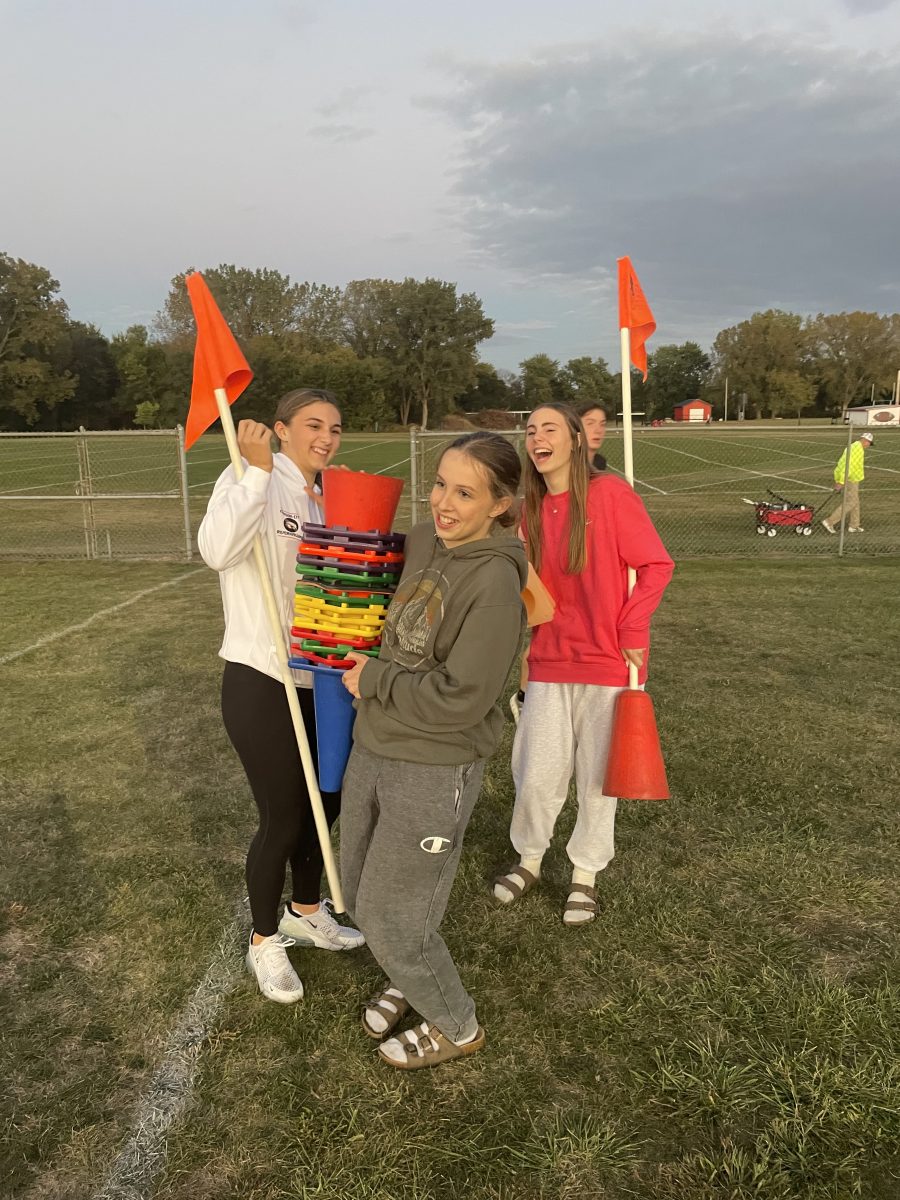 Arms full and flashing big smiles, freshmen Addie Burnett, Carleigh Arjes, and Kinnick Onder are earning Silver Cord Hours by helping pick up at the Riverhawk Invitational (Sept 24).