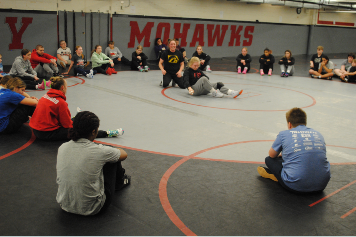 Former Mason City Wrestling Alum and current Girls' Assistant Coach, Tiffany Dickson (Sluik) demonstrates a wrestling maneuver with senior Kallie Gibbons as the team watches. Dickson is a 3x All-American. 