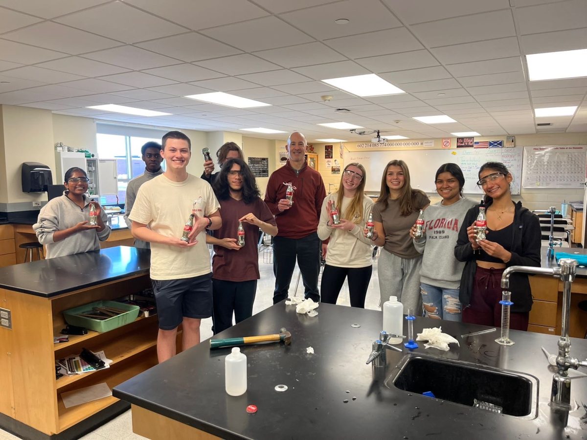 The AP Chemistry class poses with their newly-silvered Coca-Cola bottles upon completion of their lab on Wednesday. 
L to R: Kaitlyn Thangaraj ('26), Justin Nkazi ('25), Timothy Dietrich Ⅱ ('25), Landon Arhart ('25), Javier Alarcon-Newman ('25), Adam Callanan (instructor), Elise Dykstra ('26), Kate Kotta ('26), Sthepanny Torres ('26), and Sofia Ahari ('26). Not pictured: Sam Marenge. Photo courtesy of Kate Kotta. 