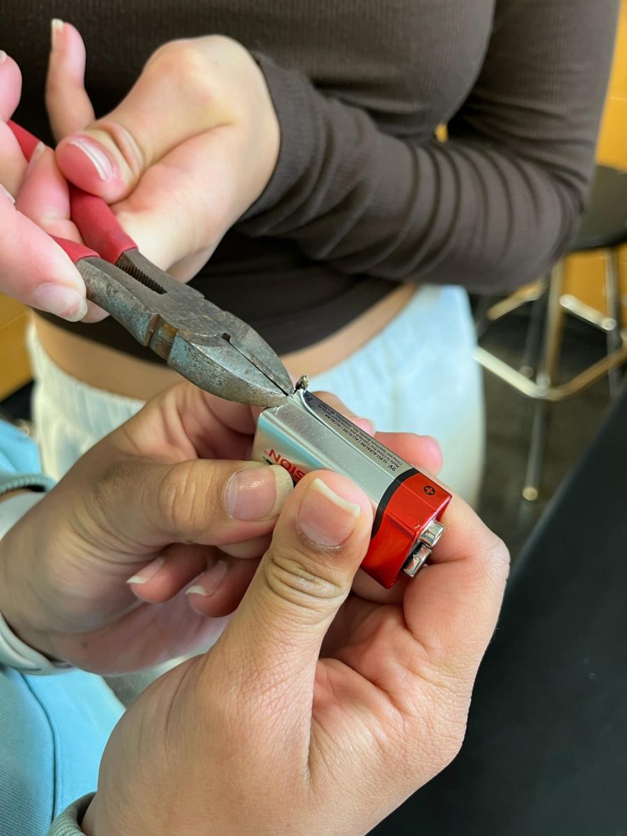 Kate Kotta and Sthepanny Torres work together to remove the metal covering on the battery. 
